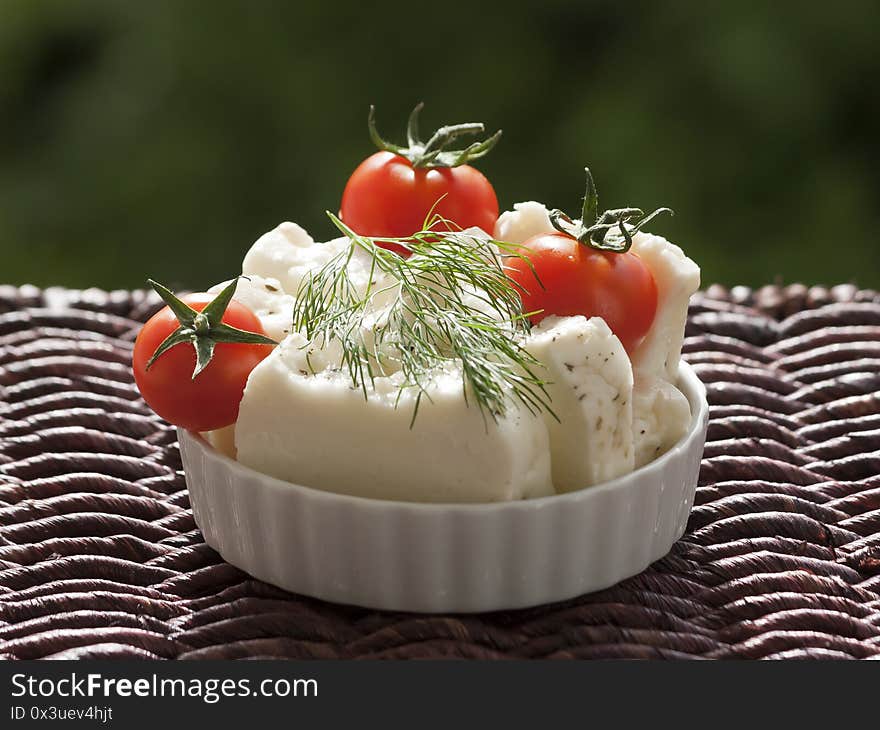 Small bowl with three cherry tomatoes and slices of Cypriot halloumi cheese with fresh dill leaf on a garden table in sunlight. Small bowl with three cherry tomatoes and slices of Cypriot halloumi cheese with fresh dill leaf on a garden table in sunlight