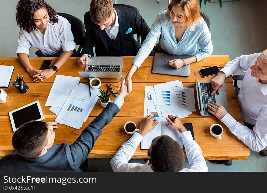 Business Partners Shaking Hands Sitting At Table In Office, Above-View