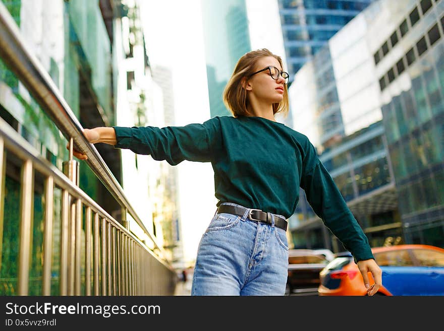 Horizontal portrait of a stylish girl with short hairstyle, in casual clothes, looking down in profile, is held by the railing