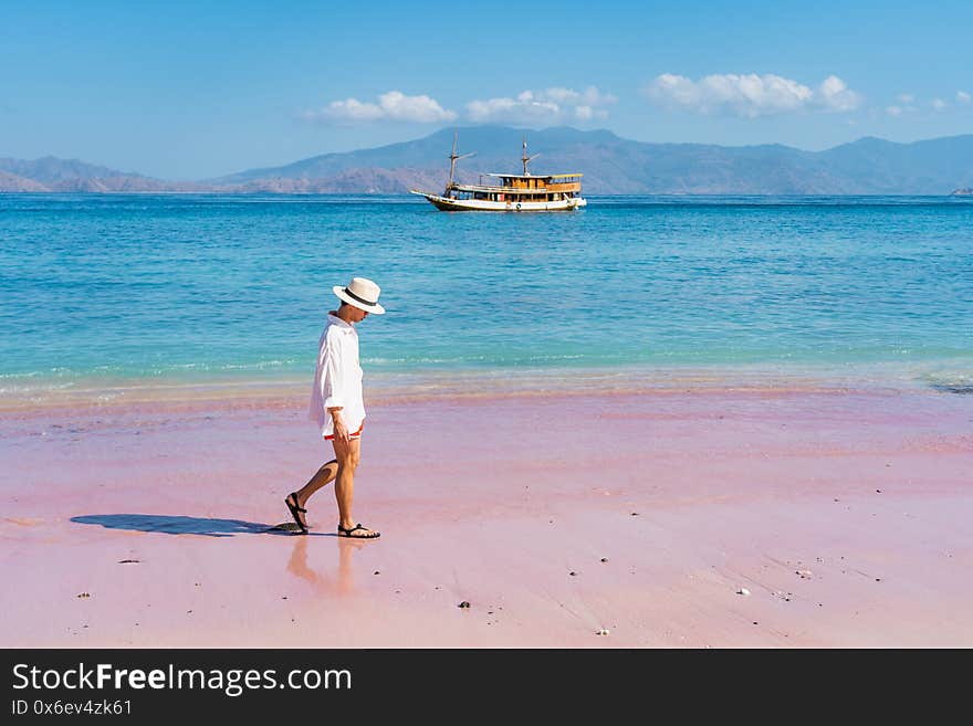 Young Asian man  traveller wearing white shirt and walking on pink beach in Komodo national park, Flores island in Indonesia