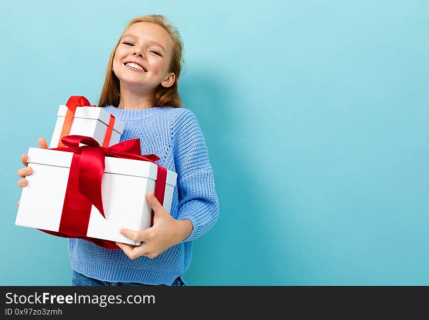 Beautiful caucasian girl holds a white boxes with gifts and rejoices isolated on blue background