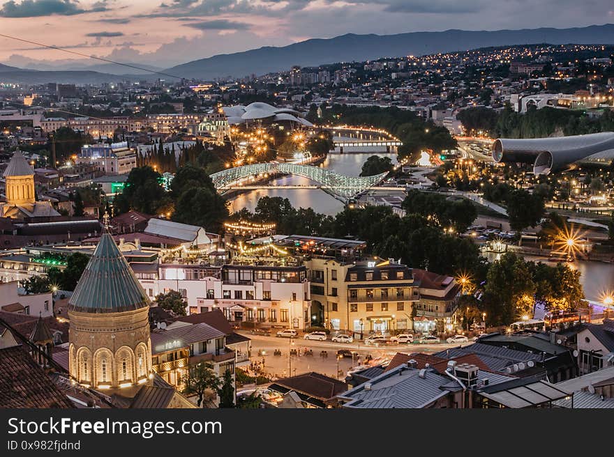 Beautiful panoramic view of evening Tbilisi, capital of Georgia. City colorful lights, river,cathedral,old buildings at a nice sunset mountains in the background.Evening city scene