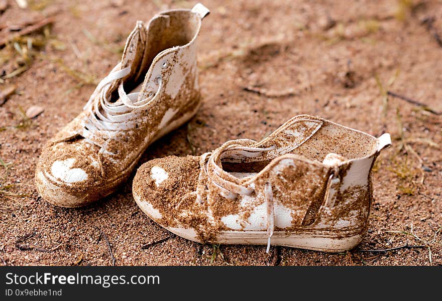 Dirty lost white sneakers shoes lays in sand . High quality photo