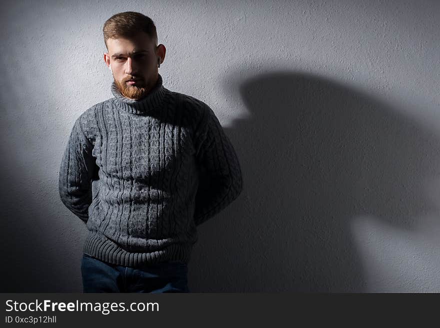 Studio portrait of a young bearded guy of twenty-five years old. In a warm winter sweater, proudly, gray, looks away. On a black