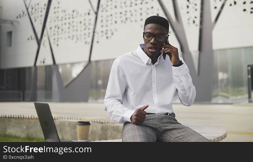 Serious African Businessman with glasses talking on cell phone in city park