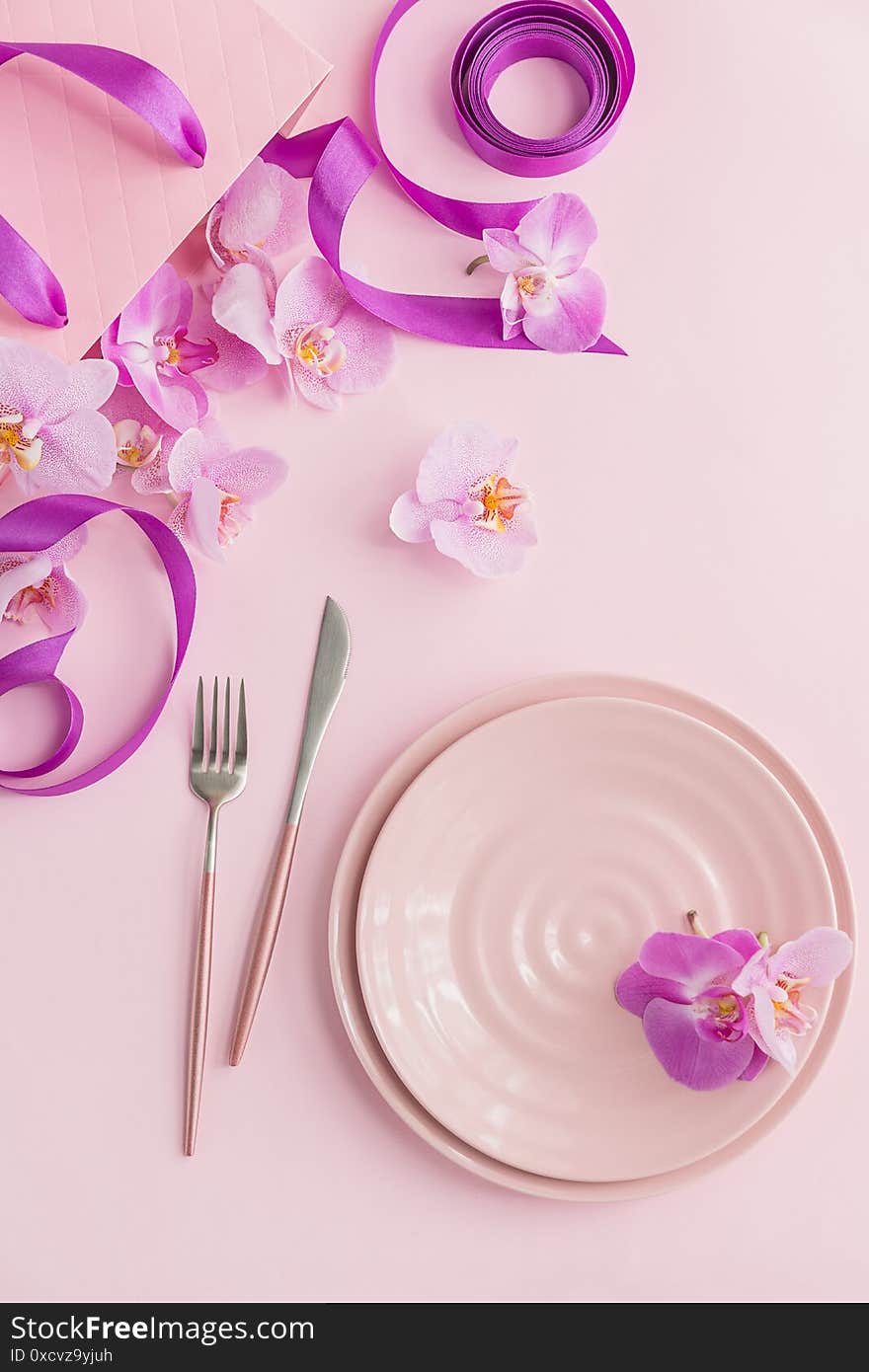 Flower and table settings overhead composition on light pink background. Pink ceramic plates, cutlery, pink gift bag with purple