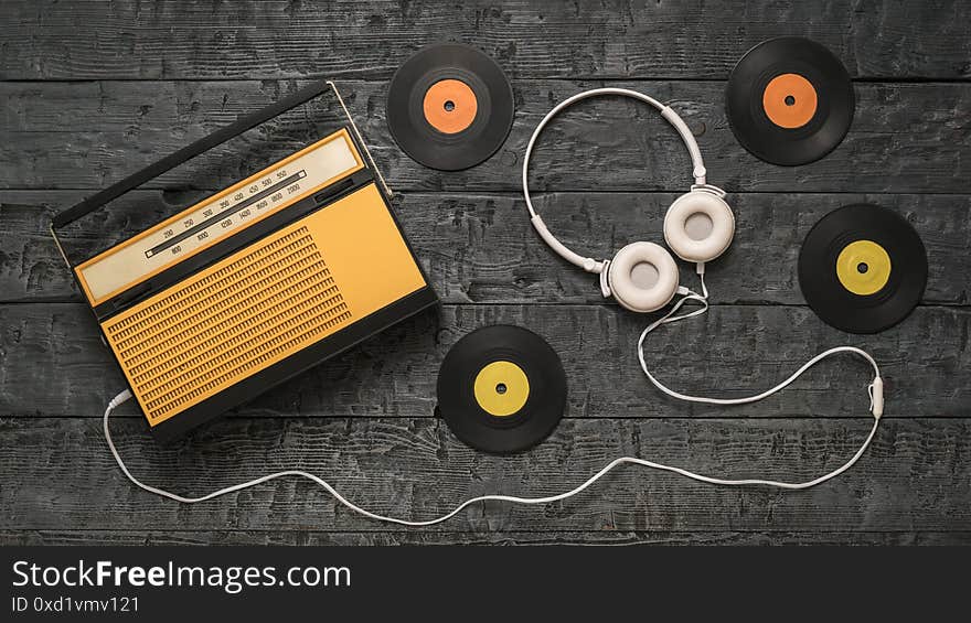 Four vinyl discs, a radio and headphones on a wooden background. Radio engineering of the past time. The view from the top