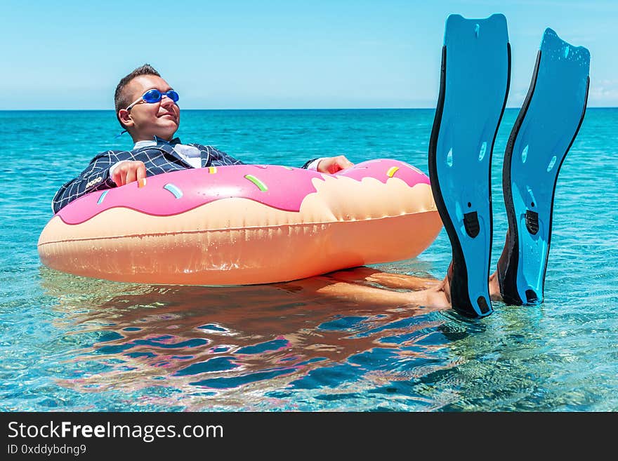 Happy businessman in flippers on an inflatable donut in the sea. Summer vacation concept