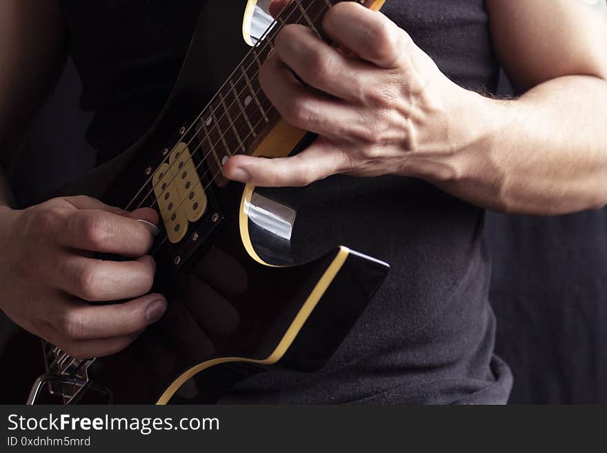 Closeup to a man wearing a black t-shirt playing a black and yellow electric guitar with wooden background. Rock & roll and music concept