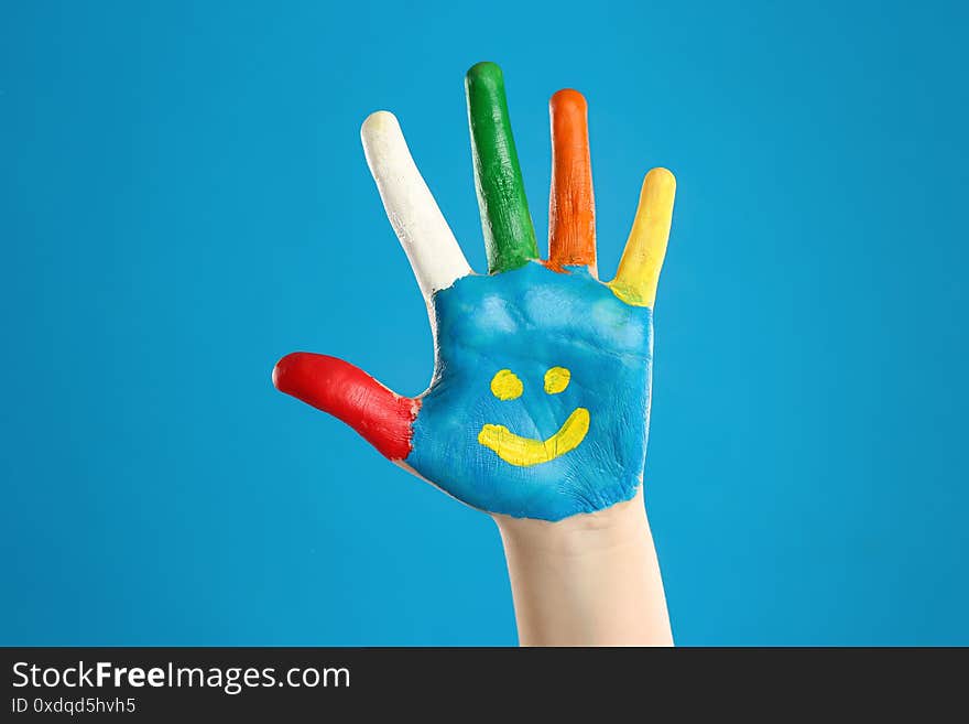 Kid with smiling face drawn on palm against blue background, closeup