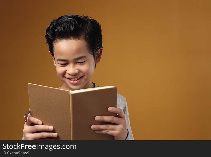 Portrait of smart young Asian student boy smiling when reading a book, education concept, against yellow background