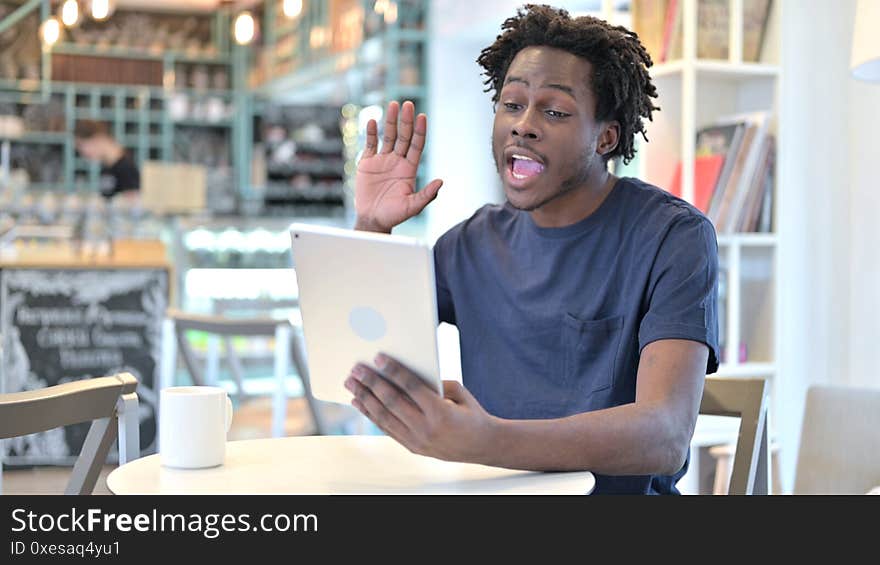 Happy African Man doing Video Chat on Tablet in Cafe