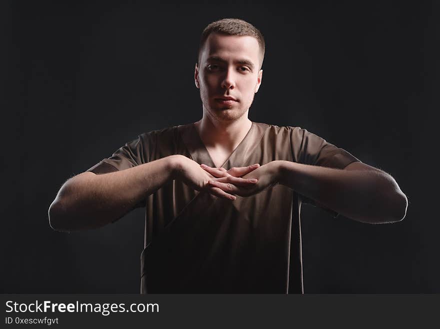 Young professional massage therapist flexes his hands before massage while standing against a dark background.