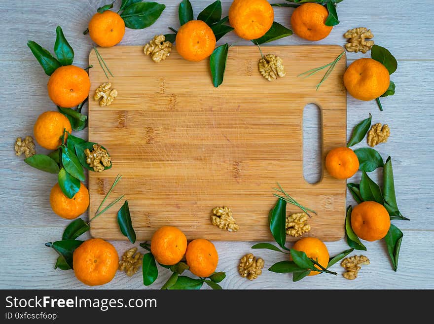 Bright orange mandarins with green leaves and walnut bright frame on light wooden board. Bright orange mandarins with green leaves and walnut bright frame on light wooden board