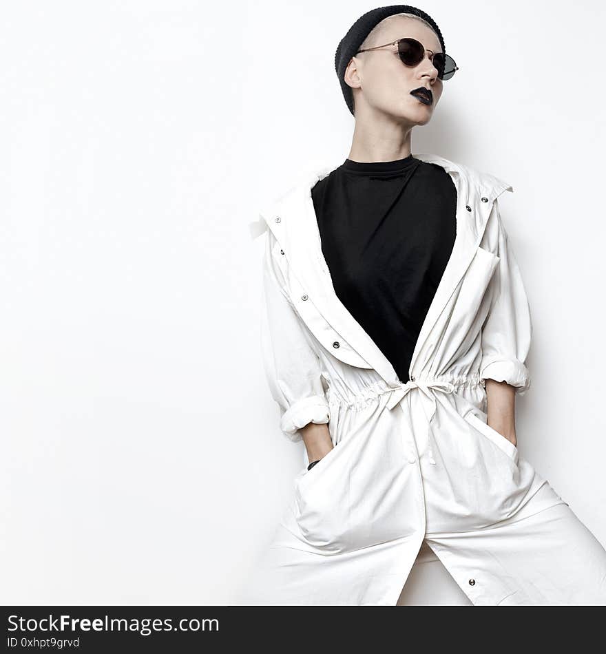 Hipster model. Swag. Minimal style. Beanie cap and stylish sunglasses. Vintage Glamour. Trendy white coat. Outfit Black