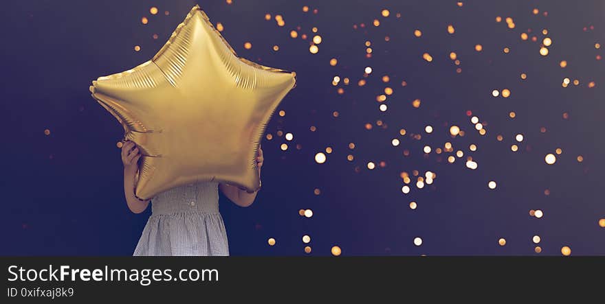 Caucasian child holding star balloon hiding face, black background