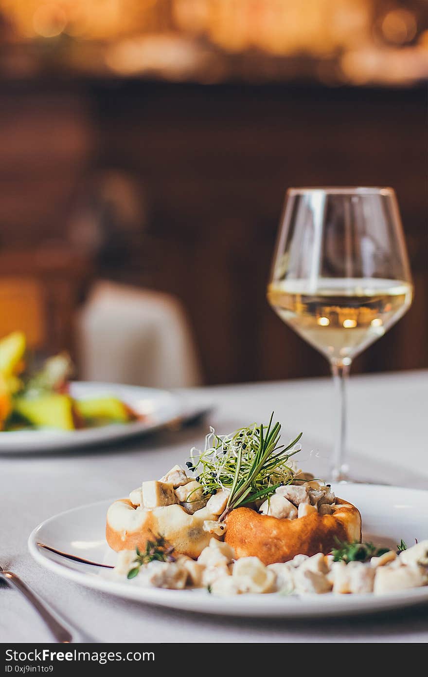 Stuffed mushrooms filled with cheese, mushroom stem and microgreen on the white plate with a glass of wine in the restaurant