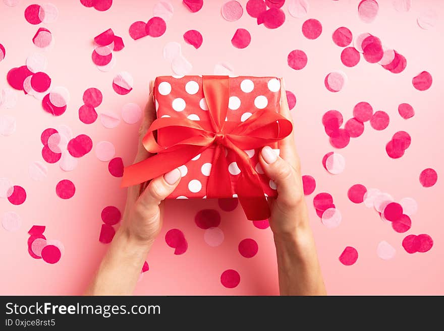 Woman hands holding red gift box top view flat lay on pink background