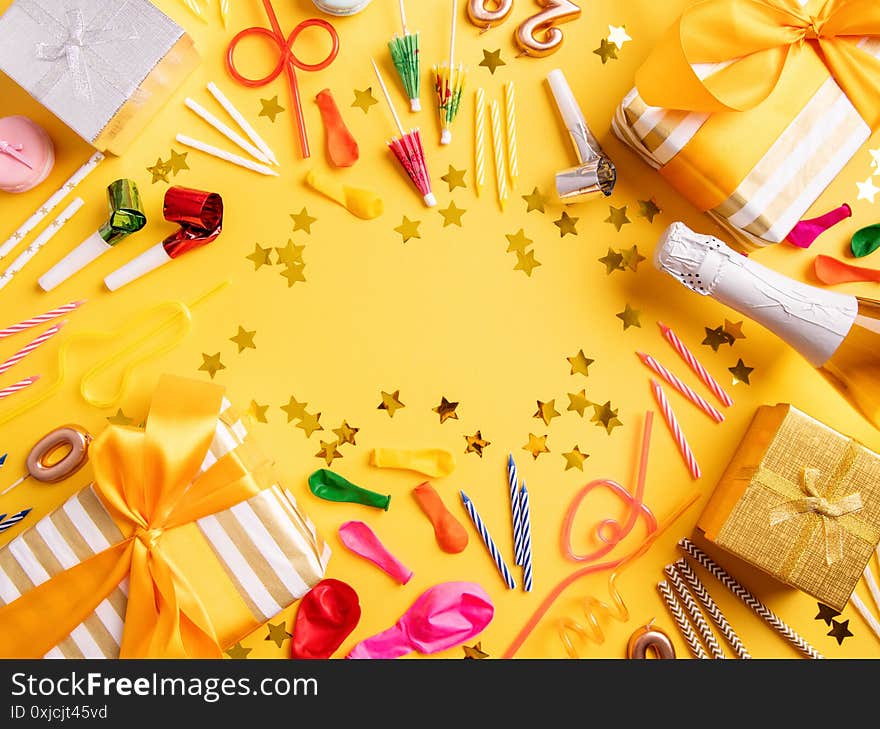 Birthday party background. Birthday supplies with party gifts, balloons, candles and confetti top view flat lay on yellow background. Birthday party background. Birthday supplies with party gifts, balloons, candles and confetti top view flat lay on yellow background