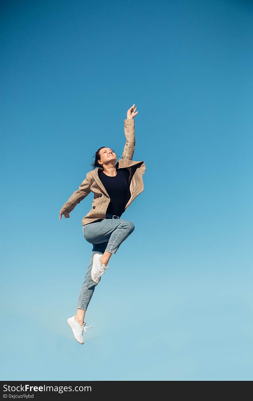 Jump in the air. A girl in full height jumps in the air having fun on a bright blue turquoise background of the summer sky color.