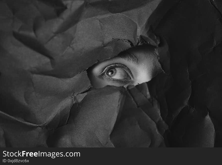 Woman`s eye in hole in black crumpled paper background, black and white concept photography for blog or poster. High quality photo