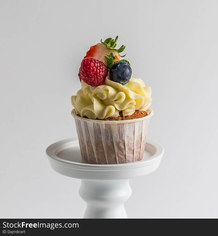 Close up, macro. Biscuit sweet raspberries, strawberries and blueberries muffins on white background. Top decorated with a cream hat with berries. Close up, macro. Biscuit sweet raspberries, strawberries and blueberries muffins on white background. Top decorated with a cream hat with berries.