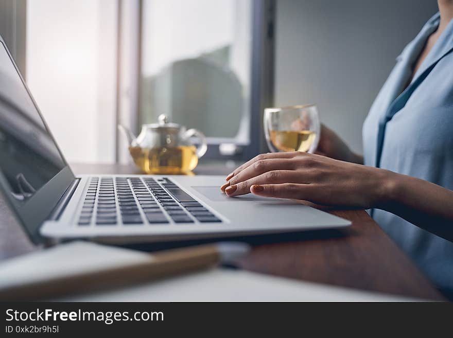 Close up of female hand touching laptop touchpad while lady sitting at the table and holding cup of tea. Close up of female hand touching laptop touchpad while lady sitting at the table and holding cup of tea