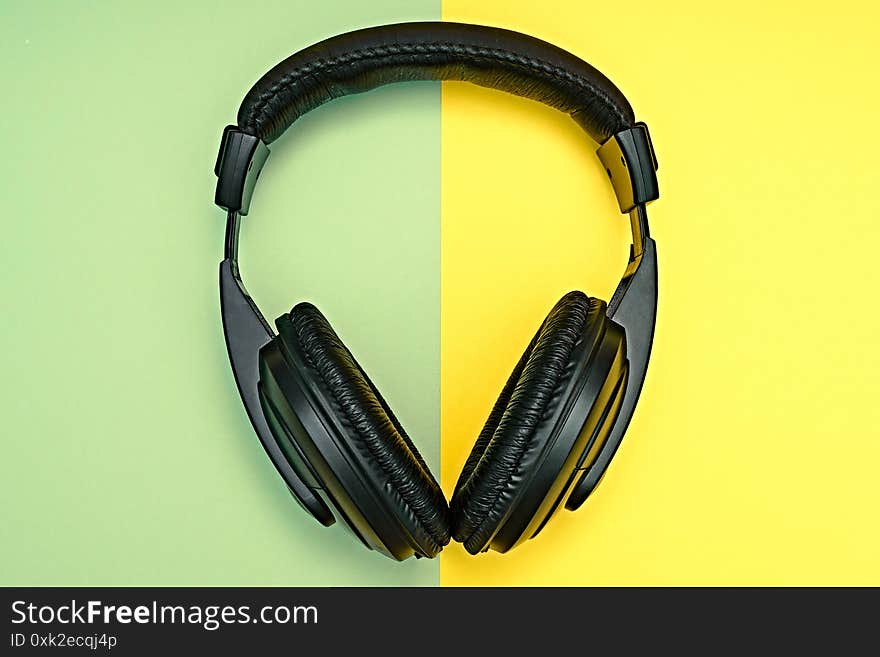 Large, black headphones lie on a colored background. Device for individual listening to music.