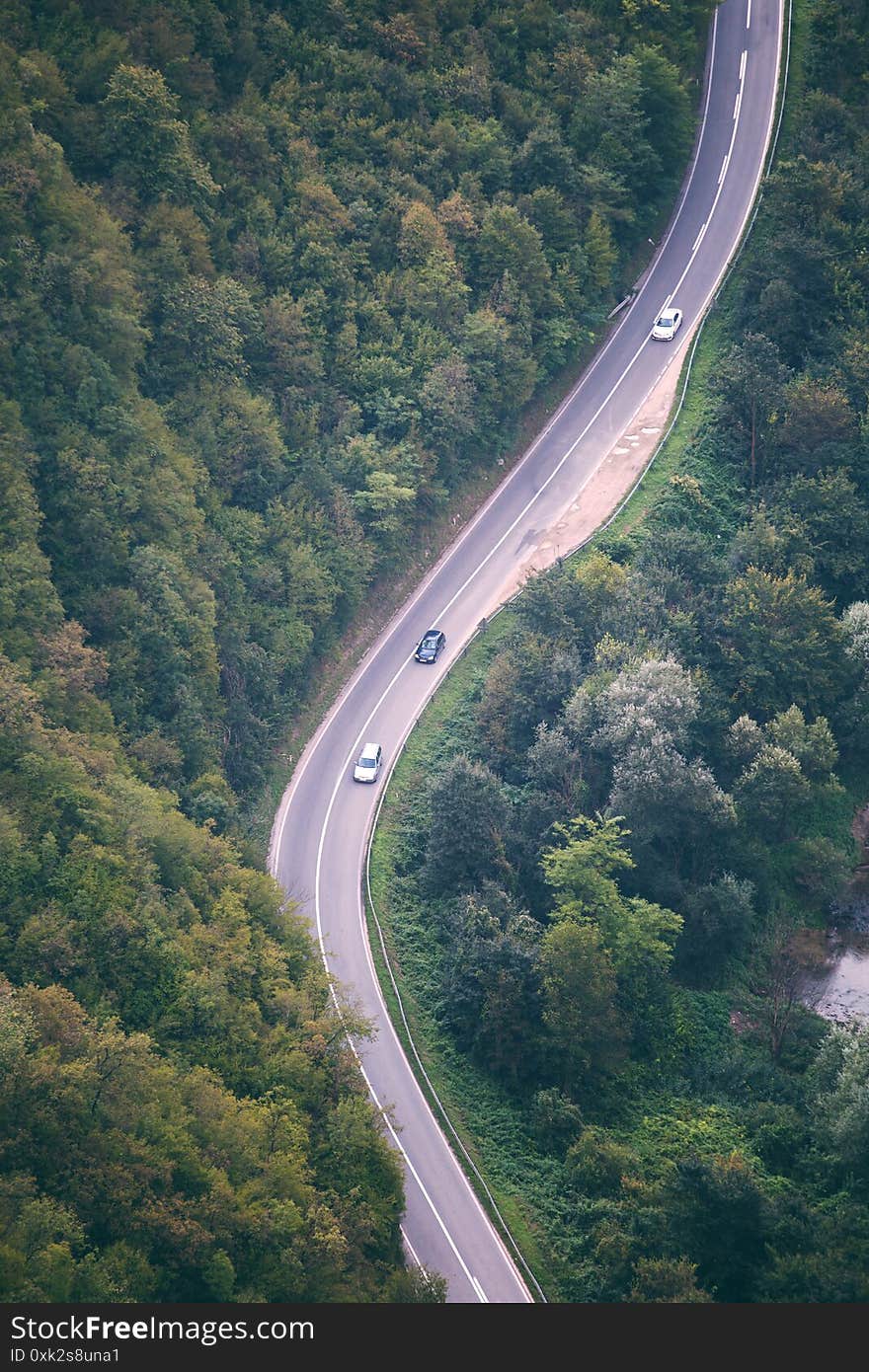 Highway through the forest aerial view. Asphalt road in the mountains. Transport connection. Cars on the road. The path through the forest