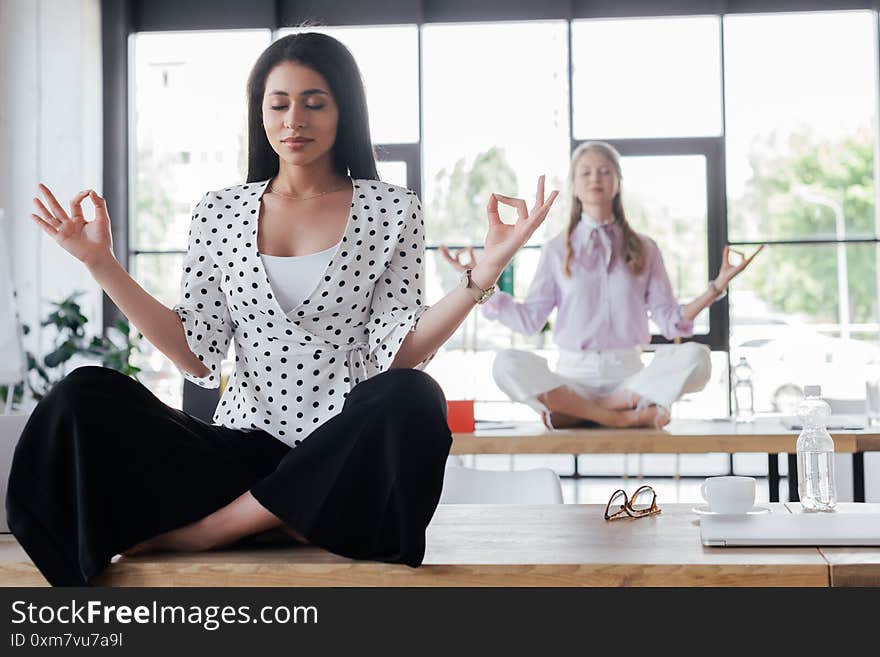 Selective focus of attractive businesswomen with closed eyes meditating in office