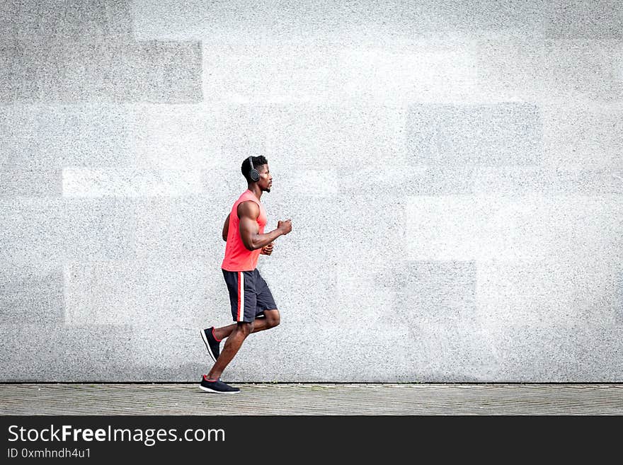 African American guy runner runs fast forward against the background of the city wall, sports man train on the street, general plan