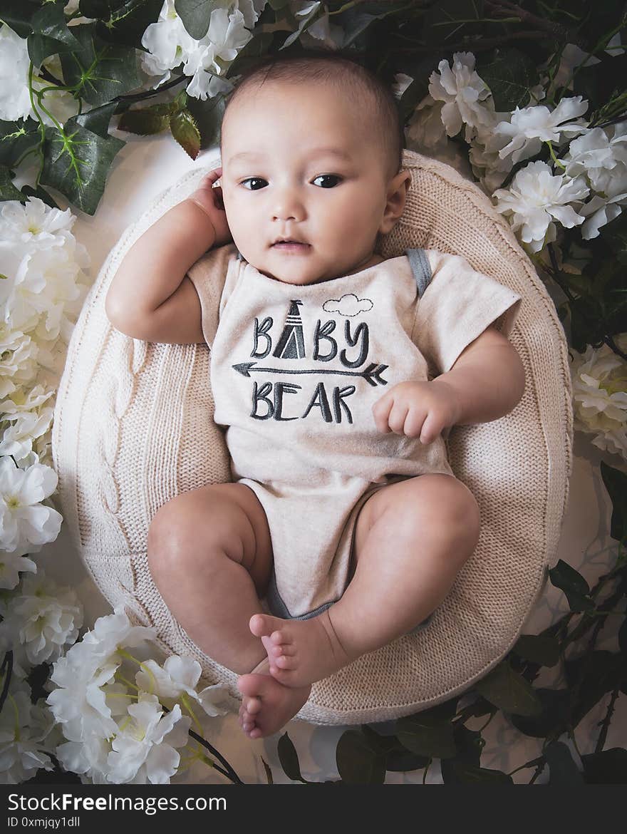 A top view of a cute Caucasian baby boy in a basket surrounded by flowers