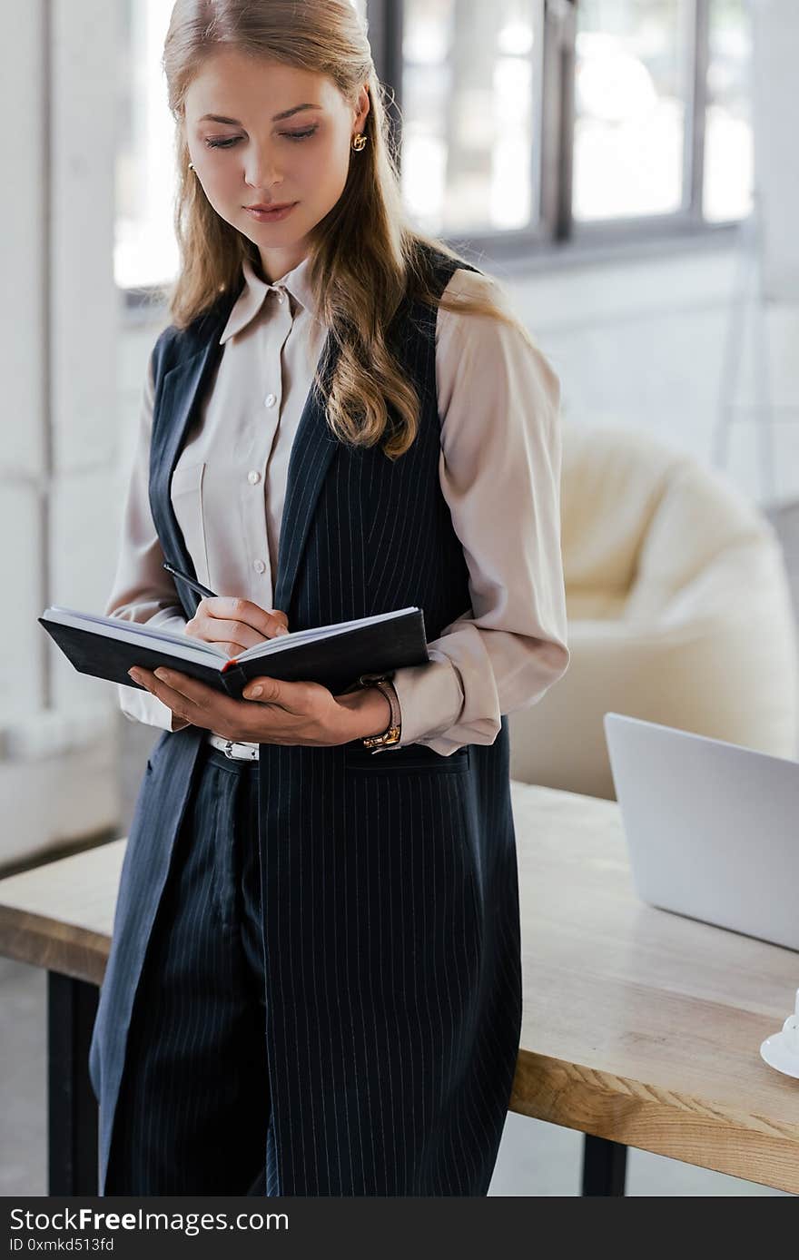 Beautiful businesswoman standing near table and writing in