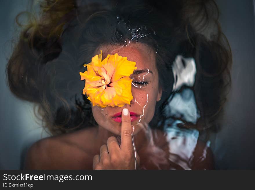 Horizontal shot of a caucasian female with her head in the water and a yellow flower on her eye