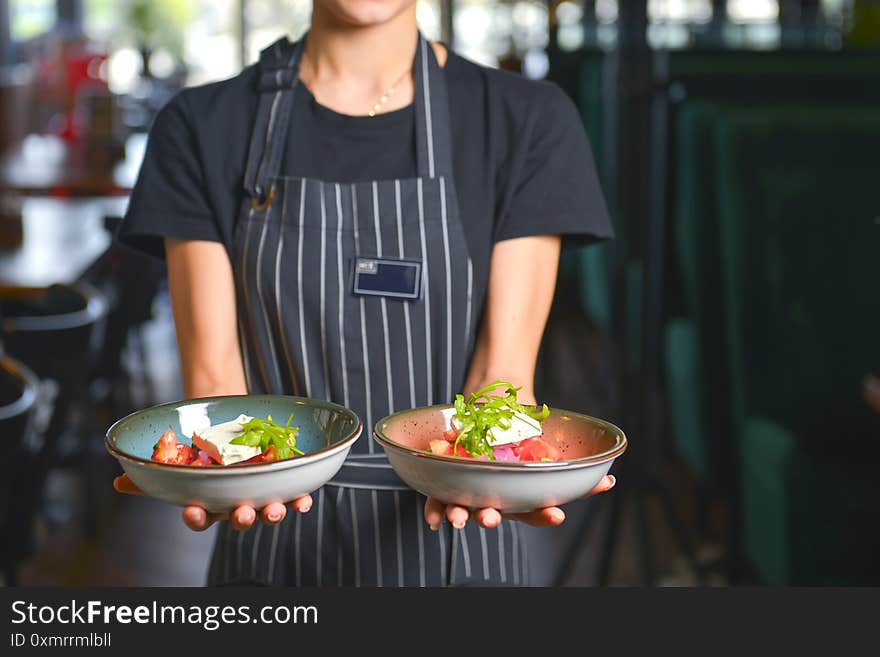 Close up of waiter serving two plates of vegetable salad with feta cheese, lettuce and tomatoes. Restaurant service