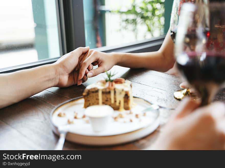 Close up hand of romantic couple holding hands dating in dessert cafe. Holding a glass of wine