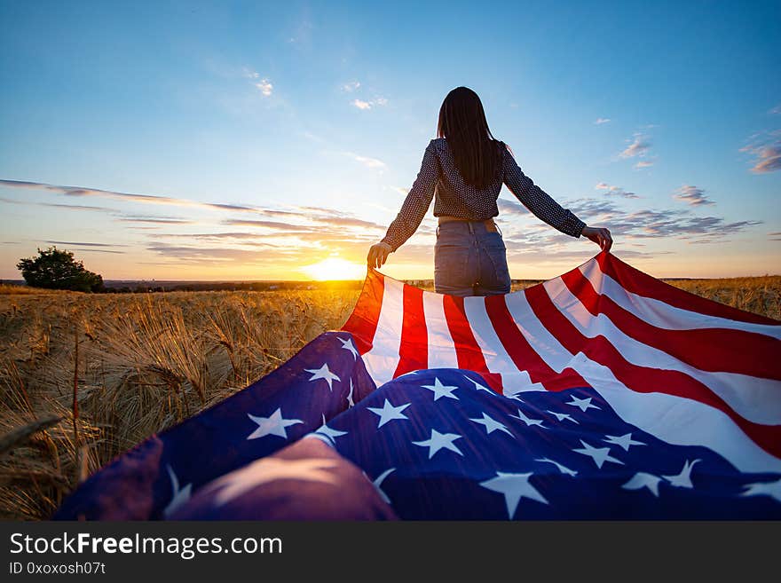 Young patriot girl with the flag of America at the wheat field