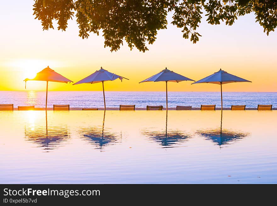 Beautiful tropical outdoor beach sea ocean with umbrella and chiar around outdoor swimming pool at sunset or sunrise time