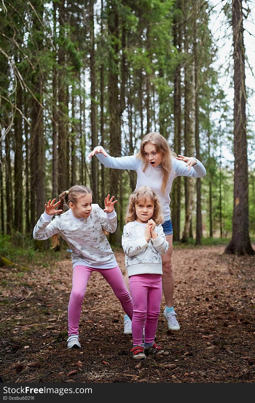 Mother and her child sister girls playing and having fun together on walk in forest outdoors. Happy loving family posing on nature landscape with with pine trees