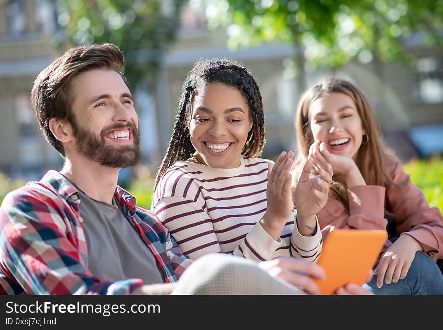 Happy and funny guy with tablet and two girls on bench.