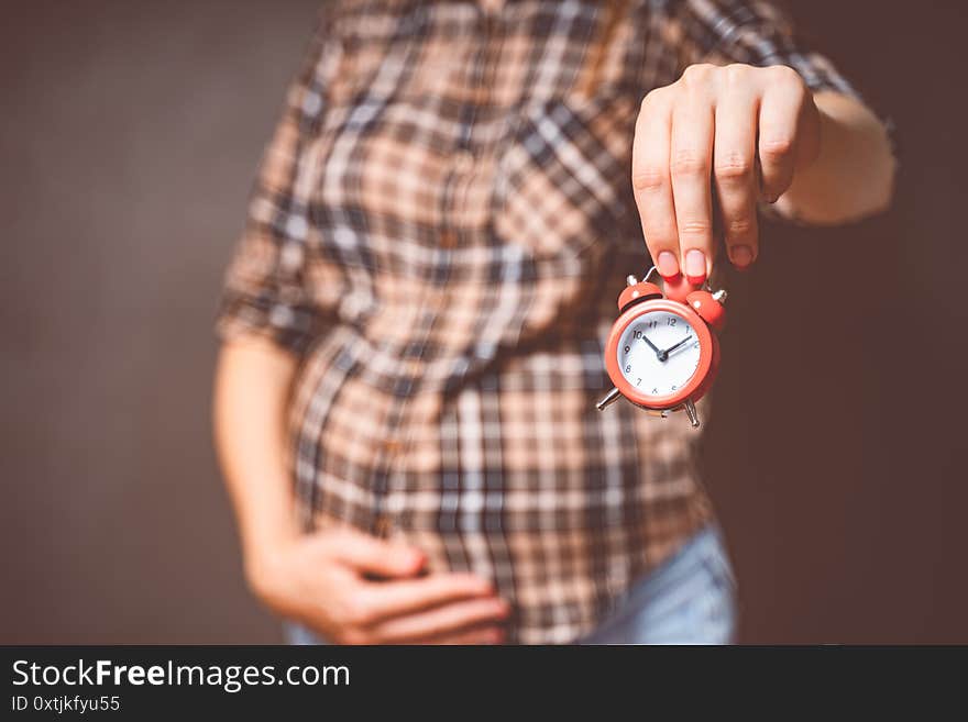 Pregnancy time concept, motherhood, people and expectation idea. Toned photo of pregnancy. Pregnant woman holds a clock