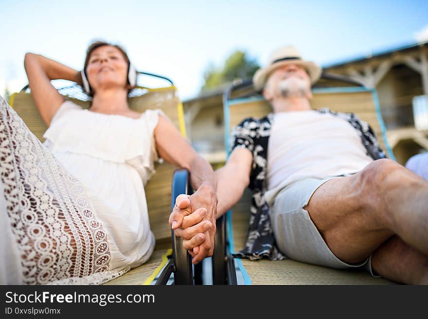 Front view of senior couple with headphones outdoors on holiday, relaxing.