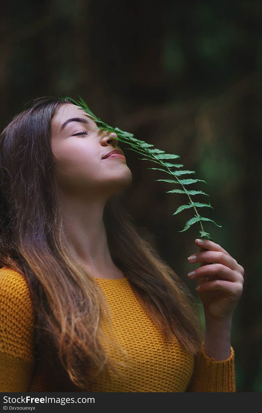 Close-up portrait of young woman on a walk outdoors in forest in summer nature, holding fern.