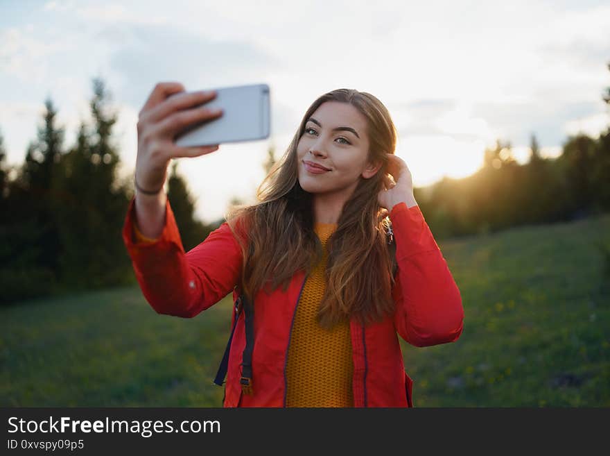 Side view of young woman on a walk outdoors on meadow in summer nature, taking selfie.