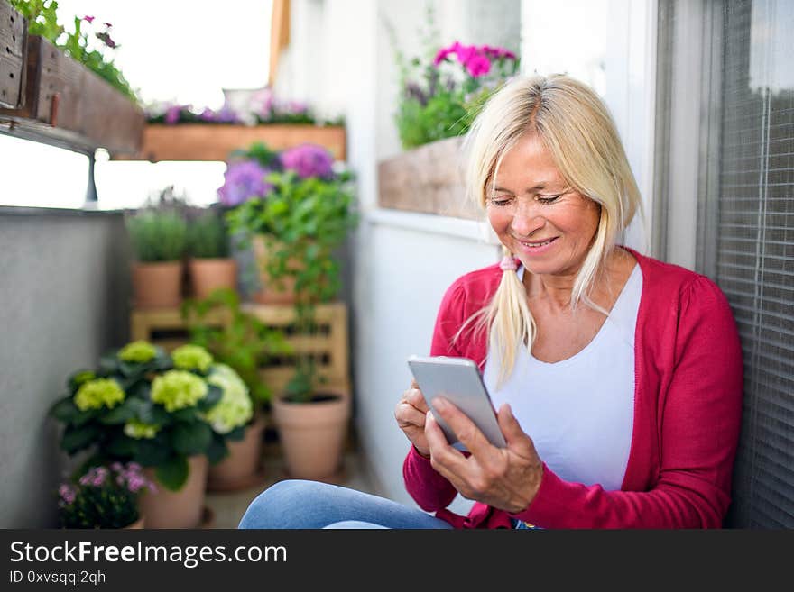 Senior Woman Relaxing On Balcony In Summer, Using Smartphone.