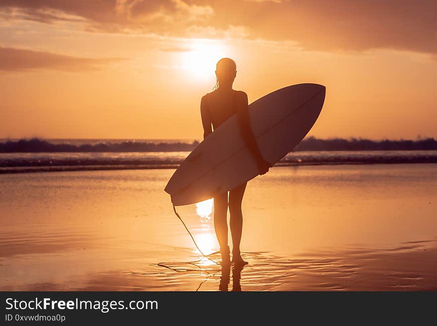 Portrait of surfer girl with beautiful body on the beach with surfboard at colourful sunset time in Bali