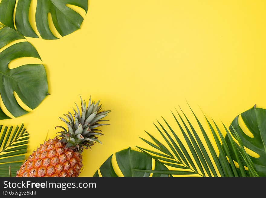 Beautiful pineapple on tropical palm monstera leaves isolated on bright pastel yellow background, top view, flat lay, overhead above summer fruit