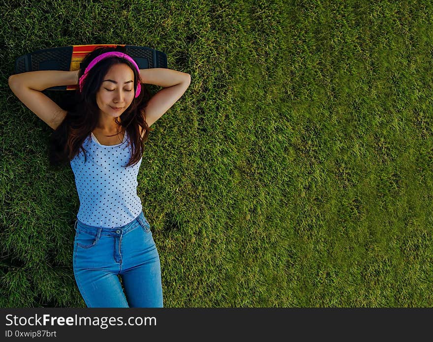 Asian Woman Listening To Music With Headphones And Laying On A Grass Field