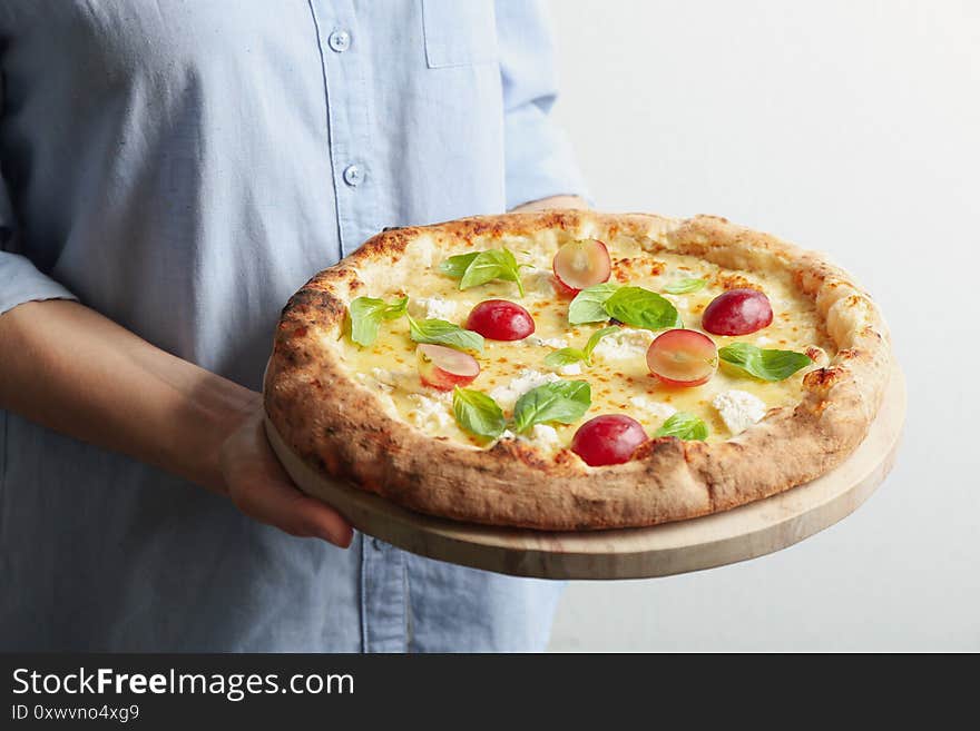 Woman holding delicious cheese pizza with grapes and basil on background, closeup