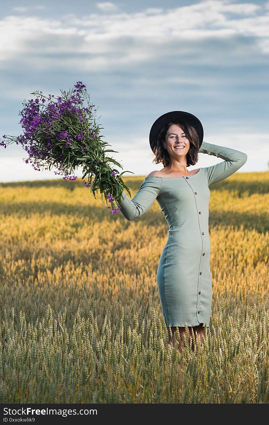 Portrait joyful young woman   brunette in blue dress   with a bouquet of purple flowers walking and resting on beautiful nature  on field. Stylish hipster woman.Outdoor atmospheric lifestyle photo. Portrait joyful young woman   brunette in blue dress   with a bouquet of purple flowers walking and resting on beautiful nature  on field. Stylish hipster woman.Outdoor atmospheric lifestyle photo